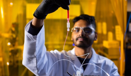 Person in lab coat holding a vial and device. 