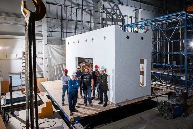 A team of researchers stand on a shake table in front of building in a research lab. 
