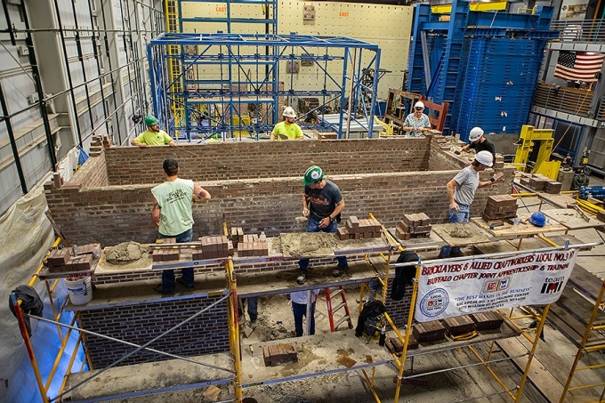 A group of people build a brick structure inside of a research lab. 