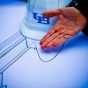 A hand gestures to a printed bridge design. A UB-branded hardhat sits on the table in the background. 