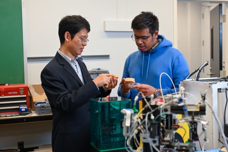 Faculty member Chi Zhou and a graduate student look at hardware in a lab. 