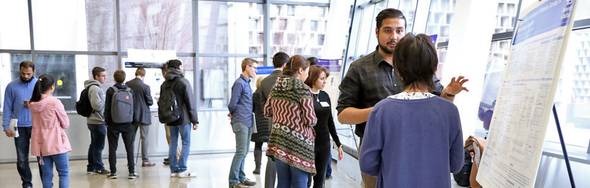 student and faculty members talk and look at posters on easels.