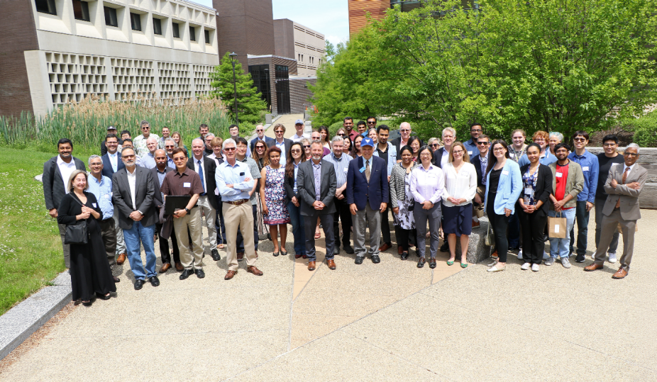 A group of symposium attendees pose together with Davis Hall and trees in the background. 