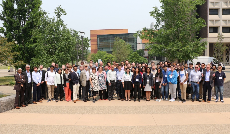 A group of symposium attendees pose together with Davis Hall and trees in the background. 