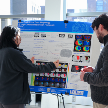 Two students discuss research in front of a poster with several figures and text. The photo is from the University at Buffalo's Mechanincal and Aerospace Engineering poster competition. 