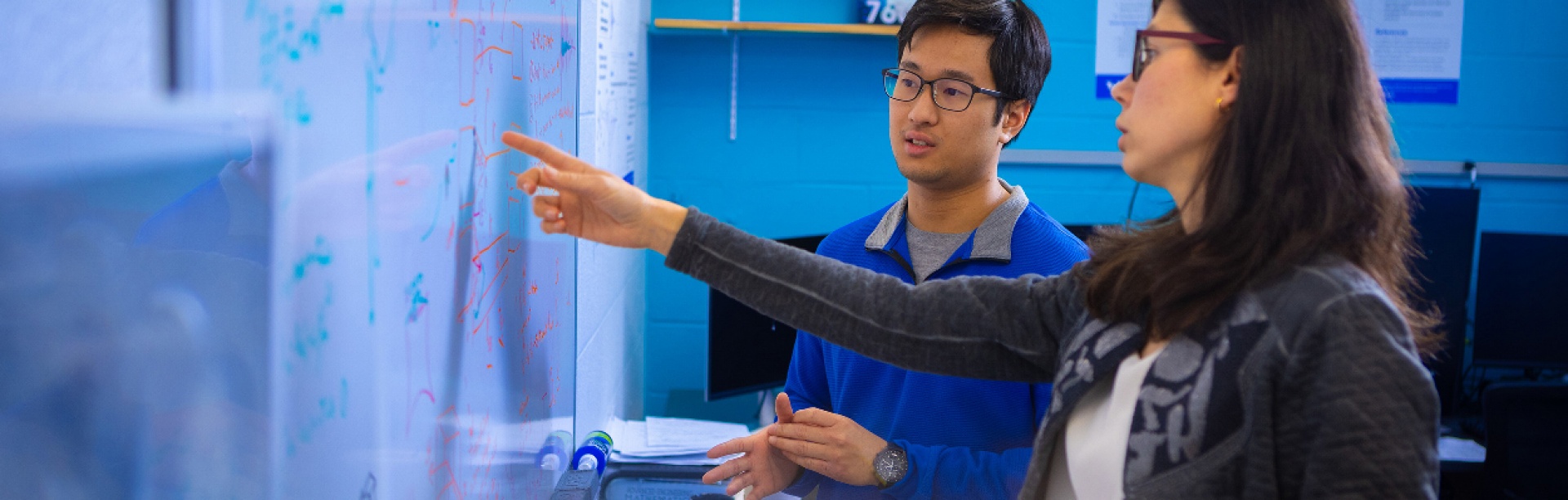 Two researchers discuss equations on a whiteboard. 