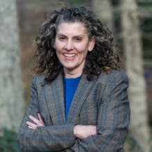 Lauri Goldkind stands smiling with her arms folded against a nature backdrop. 