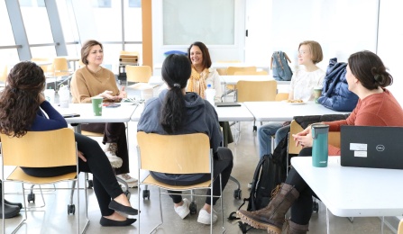 Six women sitting around a table and talking. 